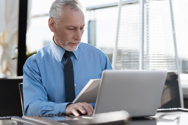 Confident bearded man looking at documents and wrinkling forehead while reading rules