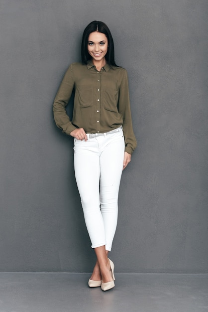 Confident and beautiful. Full length of attractive young woman in smart casual wear standing against grey background and smiling