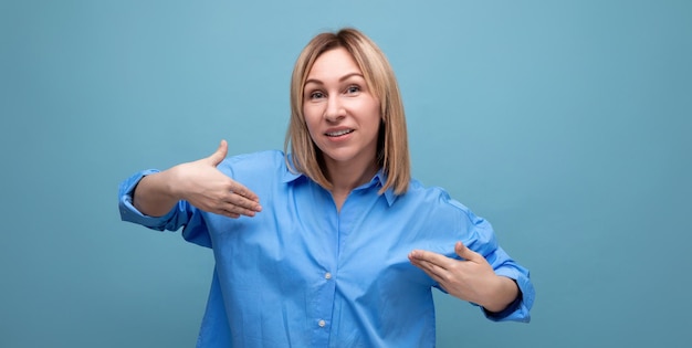 Confident blond young millennial in casual shirt showing off her look on blue background with copy