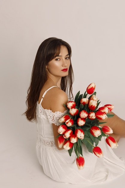 Confident brunette female with red lips dressed in white dress