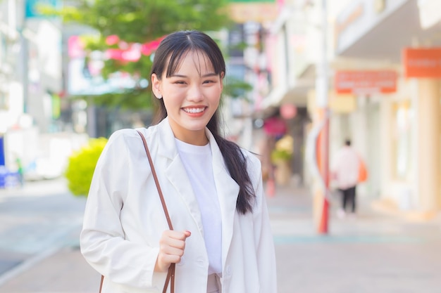 Confident business Asian working female who wears white shirt and shoulder bag while she is walking.