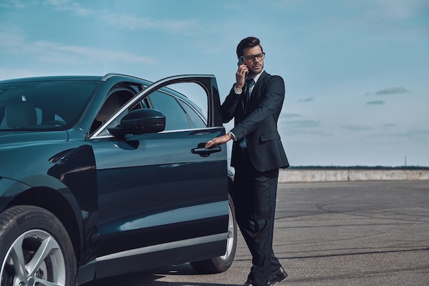 Confident business expert. Full length of handsome young businessman talking on the phone while entering his car outdoors