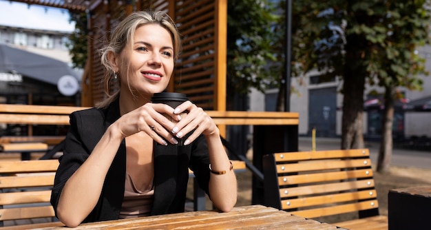 Confident business woman drinking coffee in a street cafe with a smile on her face