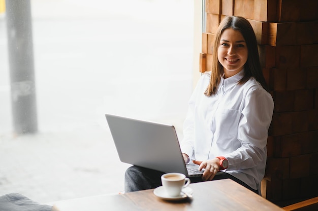 Confident business woman searching resume on site via laptop computer while sitting in restaurant during work break. Female project manager using applications on notebook device, resting in cafe