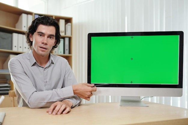 Confident businessman or coach pointing at green screen of computer