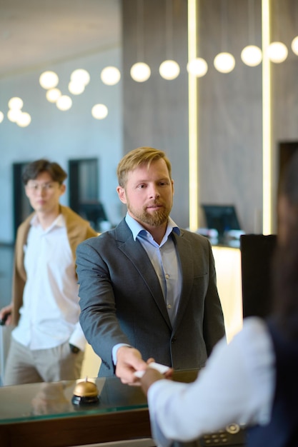 Confident businessman in formalwear taking keycard held by receptionist