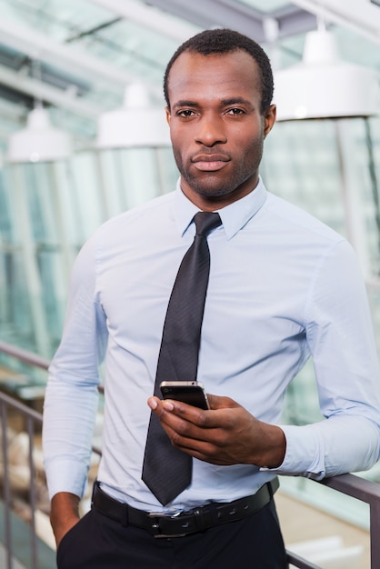 Confident businessman. Handsome young African man in shirt and tie holding mobile phone