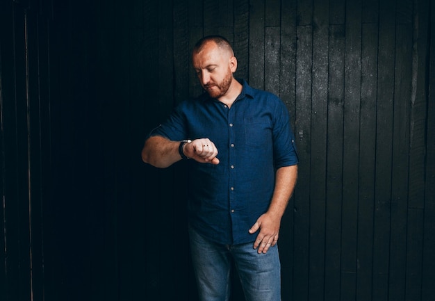 A confident businessman looks at his wristwatch on a dark wooden background