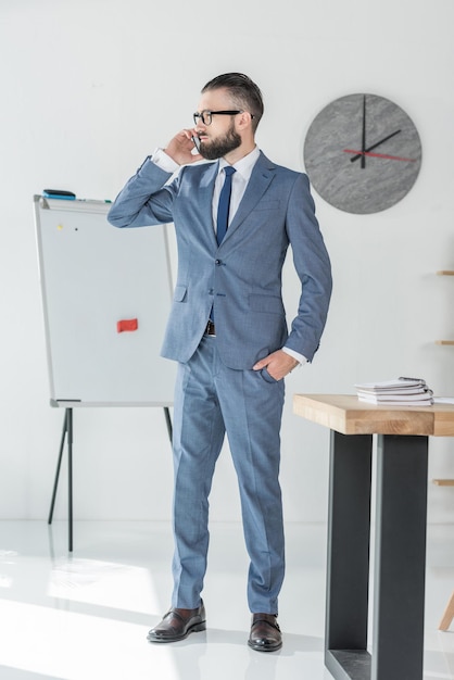 Confident businessman talking on smartphone while standing at workplace in office