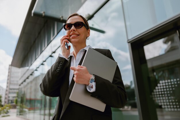 Photo confident businesswoman having a phone conversation in front of a modern office building