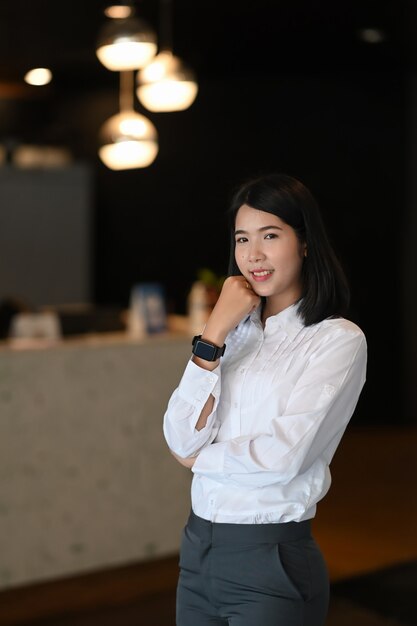 Confident businesswoman wearing smart watch standing in modern office and looking to camera.