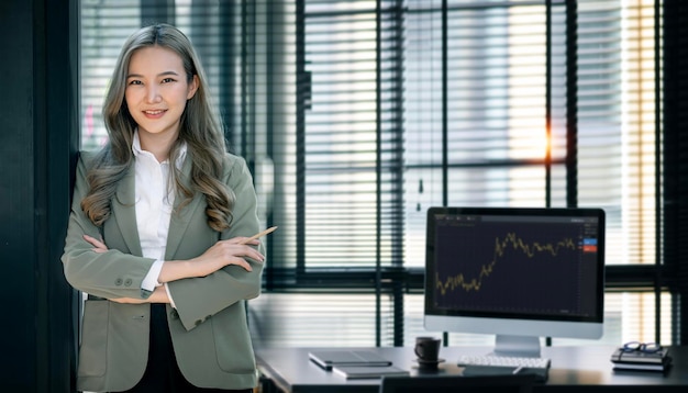 Confident businesswoman with arms crossed standing in modern dark tone office smiling to camera