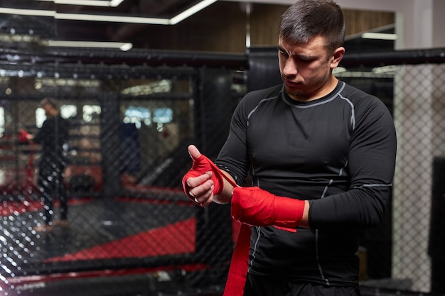 Confident Caucasian Male Kickboxer Fighter Preparing For Fight, Wrapping Hand In Red Bandage, Get Ready, Going To Train And Exercising