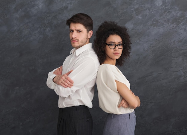 Confident couple in formal suit with crossed hands posing back to back on gray studio background, copy space