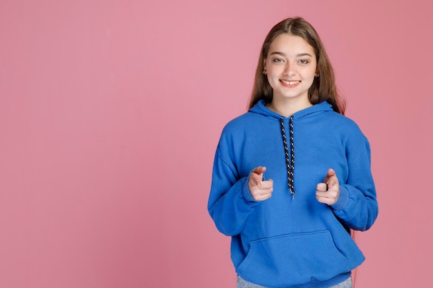 Confident cute female student pointing at camera with both hands while widely smiling at camera