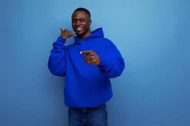 Photo confident darkskinned young american man in a blue sweatshirt shows his hand at an advertisement on