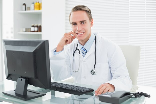 Confident doctor sitting with computer at medical office