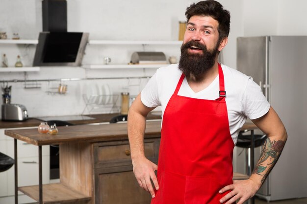 Confident and experienced chef Hipster in kitchen Mature male Bearded man cook Restaurant or cafe cook Bearded man in red apron Man chef cooking restaurant cuisine Happy bearded man in apron