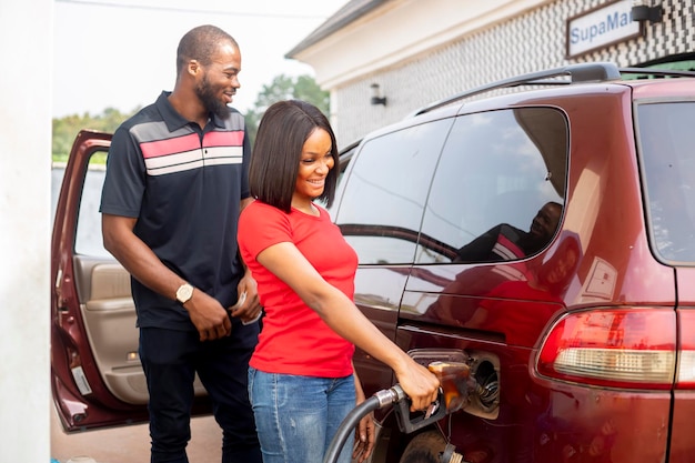 Confident female attendant talking with customer while tanking car at gas station