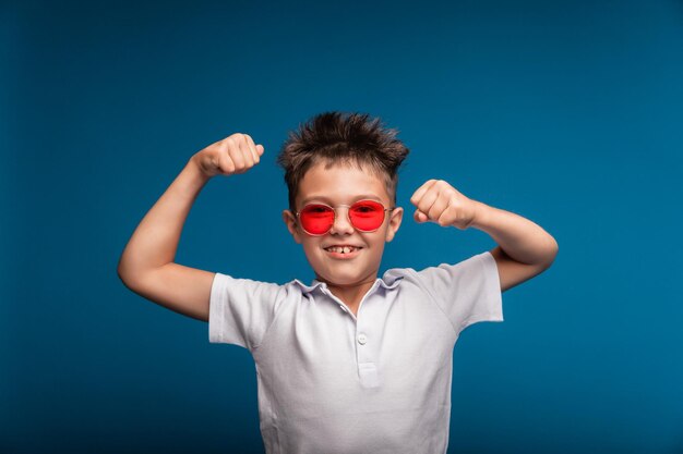 A confident guy shows his muscles A sporty child is a boy demonstrating the strength of the biceps muscles of his arm A schoolboy with glasses