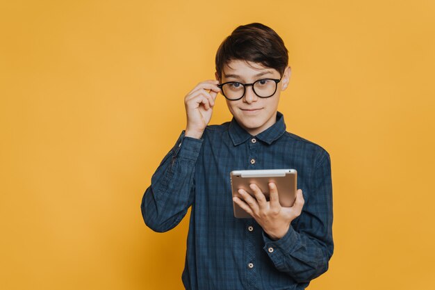 Confident handsome smart boy in glasses wearing in casual shirt holding tablet, looking interested by new knowledge. Education concept.