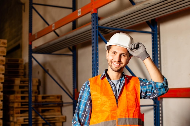 Confident handsome worker in protective hardhat and uniform at the warehouse of a industrial manufacturing. Confidence, success, business concept