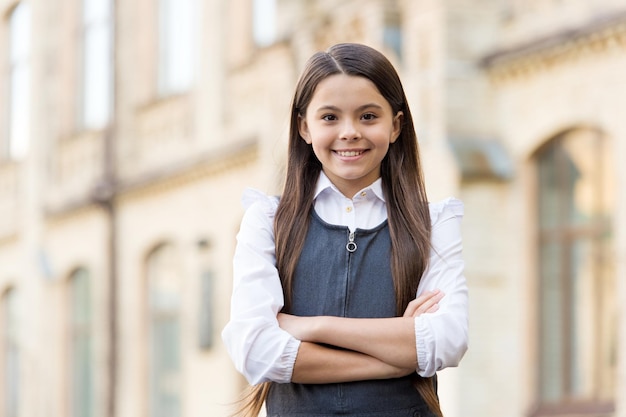 Confident happy kid smile in school uniform keeping arms crossed outdoors, confidence.