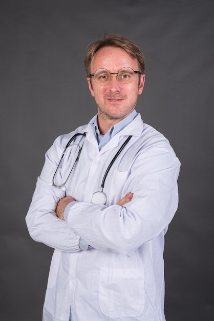 Confident male doctor smiling with arms crossed against gray background