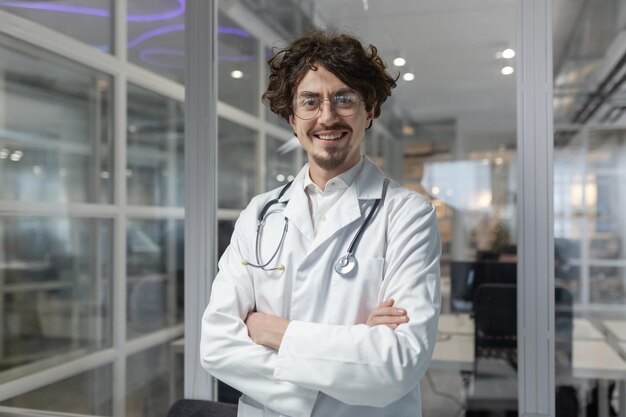 A confident male doctor in a white coat and stethoscope standing with crossed arms inside a medical