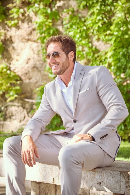 Confident male entrepreneur in elegant suit on sitting bench in park and looking away on summertime