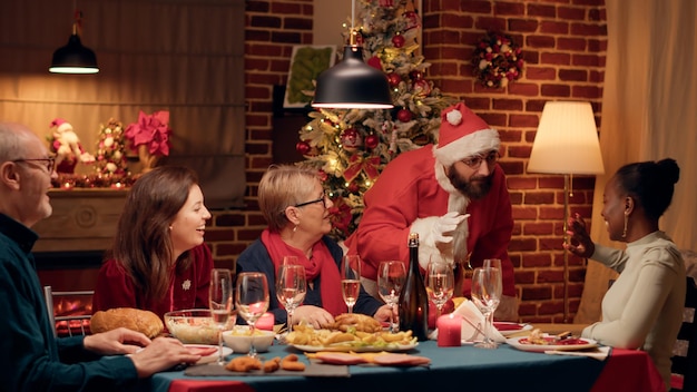 Confident man disguised as Santa showing up with gifts for everybody at winter holiday celebration. Santa Claus looking person surprising everybody at Christmas dinner when he shows up with presents.