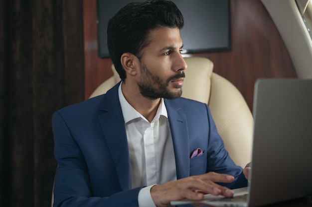 Confident middle eastern entrepreneur using laptop working online flying luxury private jet