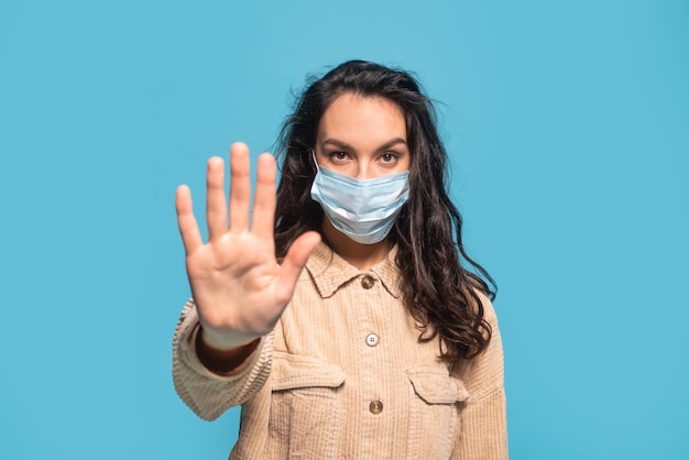 Confident millennial caucasian female brunette student in protective mask showing palm stop sign with hand