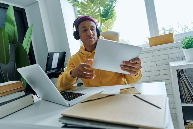 Confident mixed race man in headphones using technologies while sitting at his working place