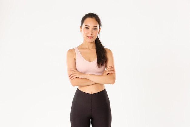 Confident and motivated asian sportswoman ready for workout, cross arms chest and smiling encouraged for productive training, white background.