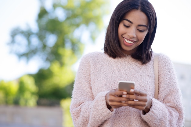 Confident nice energetic girl using her smartphone for communicating with her friends and replying them within seconds