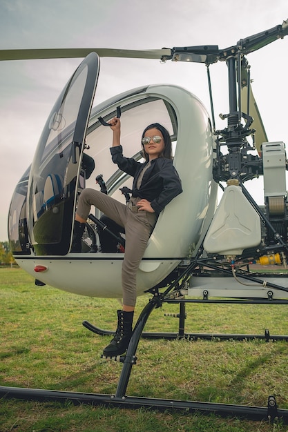 Confident preteen girl in mirrored sunglasses standing on footboard of helicopter