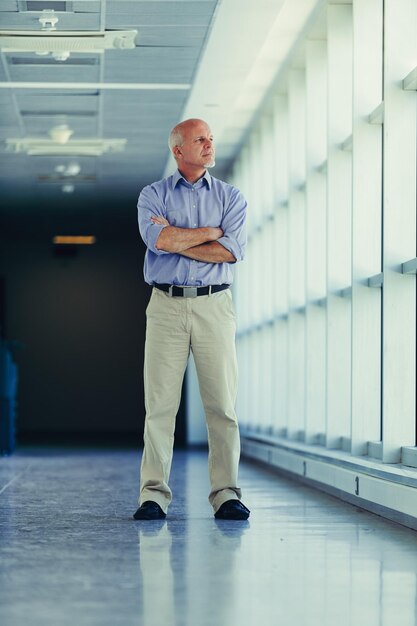 Photo confident senior businessman stands in an office corridor arms folded looking thoughtful