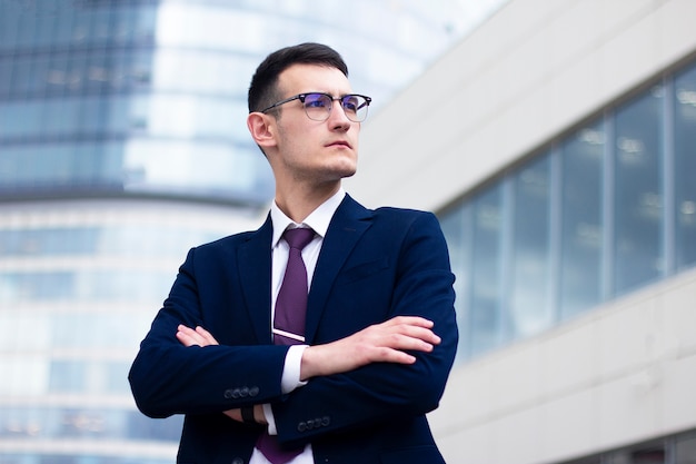 Confident serious young businessman in a formal suit and in glasses liking into distance and holding his hands