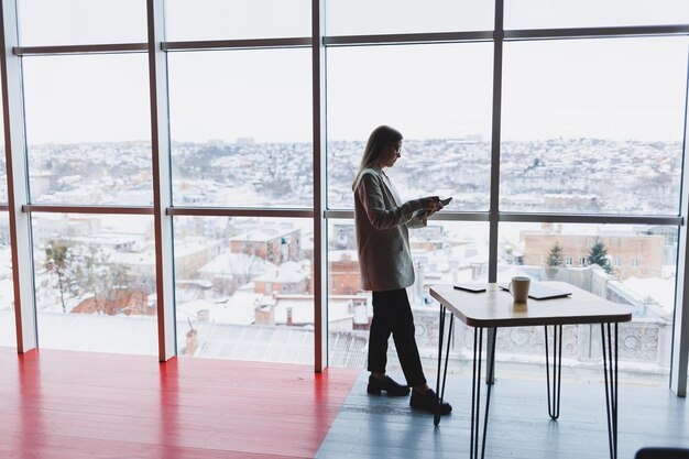 Confident slovenian business woman in elegant clothes checks notes in a notebook standing by the window in the office a serious female manager reads information viewed on a notebook