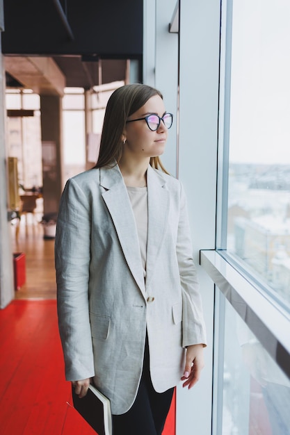 Confident slovenian business woman in elegant clothes checks notes in a notebook standing by the window in the office a serious female manager reads information viewed on a notebook