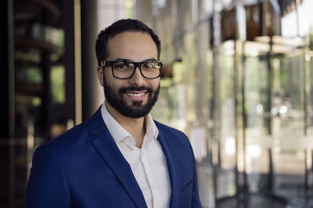 Confident smiling Arabian business man wearing eyeglasses looking at camera standing in office