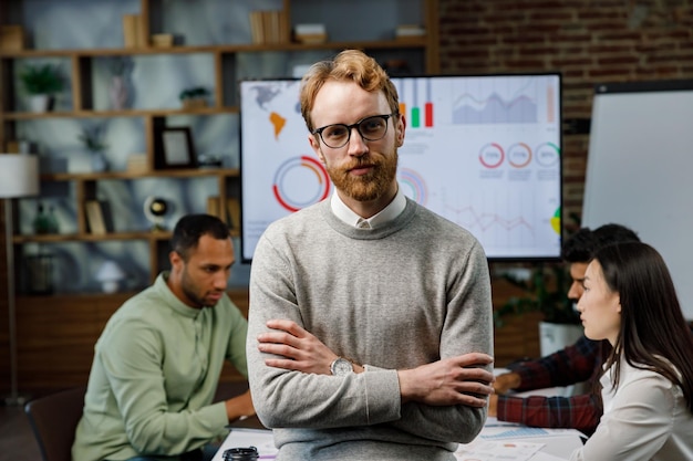 Confident smiling ginger guy startup team leader standing in front of mixed race office workers or b