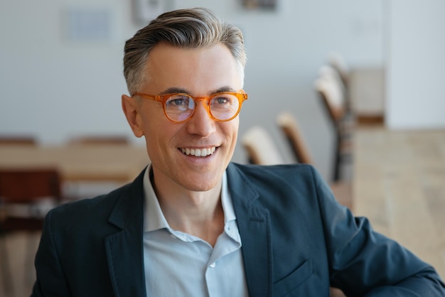 Confident smiling mature businessman wearing stylish eyeglasses sitting in modern office