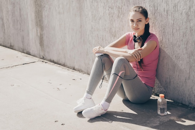 Confident sports girl sitting on the ground outdoors resting after training and gaining strength