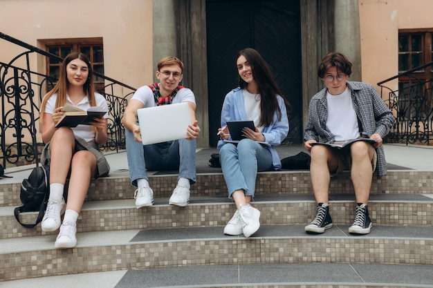 Confident students Group of happy young people working together and looking at laptop while sitting on steps