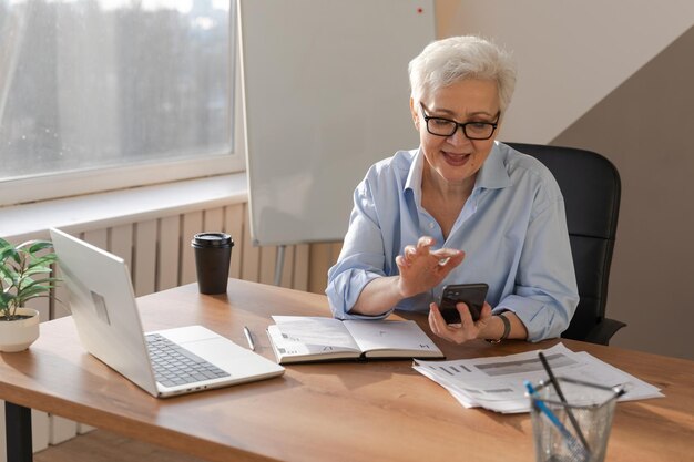 Confident stylish european middle aged senior woman using smartphone at workplace stylish older matu