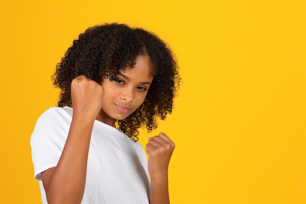 Confident teen curly girl in white tshirt shows fists ready to fight with bullying