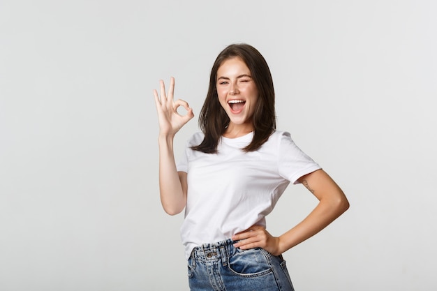 Confident and upbeat attractive girl showing thumb-up gesture in approval.