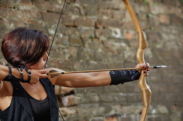 Confident woman shooting from bow, tacking focus, looking away.